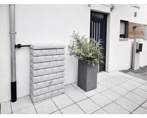 Wassertank in Steinoptik neben Fallrohr und Pflanzgefäß vor einem Haus