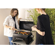 Zwei Frauen grillen Gemüse und Fleisch auf einem tragbaren Grill im Freien.
