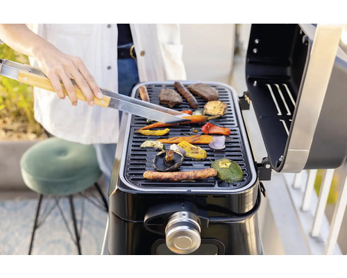 Person grillt Gemüse und Fleisch auf einem Grill.