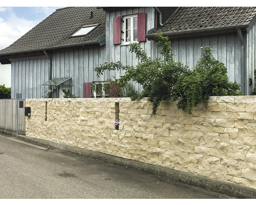 Eine Mauer aus Natursteinen vor einem Wohnhaus.