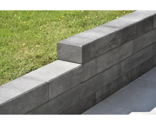 Gestapelte graue Gartenmauersteine aus Beton mit Rasen im Hintergrund.