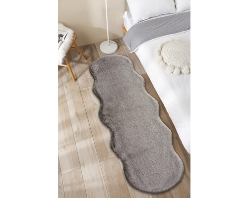 Innenaufnahme eines Schlafzimmers mit einem Bett und einem grauen Teppich in Felloptik.