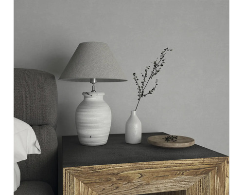 Dekorative Tischleuchte mit Lampenschirm neben einer Vase mit Zweig auf einem Nachttisch