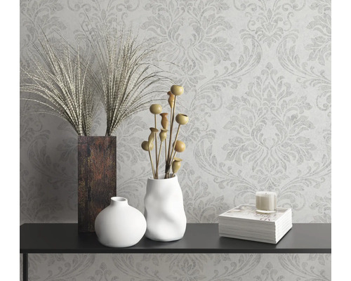 Dekoratives Stillleben mit Vasen, Zierpflanzen, Kerze und Buch auf einer Konsole vor einer gemusterten Tapete