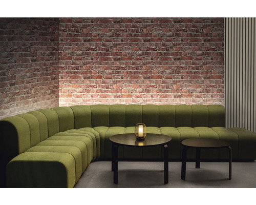 Raumansicht mit grünem Modulsofa, zwei runden Tischen und Ziegelwand