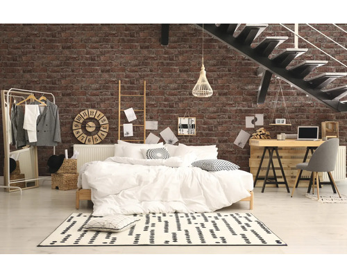 Schlafzimmer mit Bett, Schreibtisch und Treppe vor einer Ziegelwand