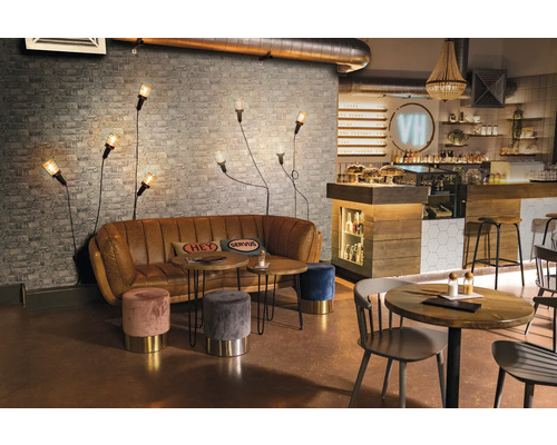 Innenraum eines Cafés mit Sofa, Tischen, Hockern und Wandleuchten vor einer Ziegelwand