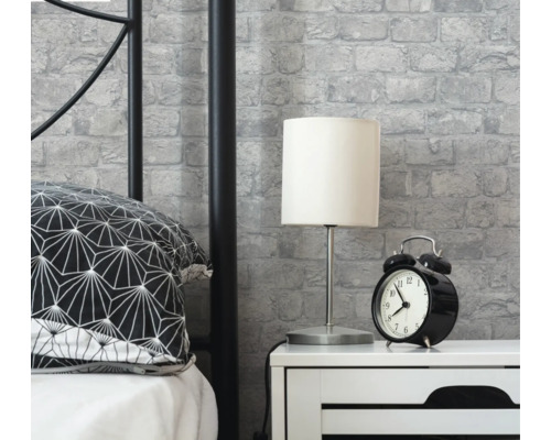 Schlafzimmerszene mit Bett, Nachttisch, Lampe, Wecker und Mauerwerkstapete