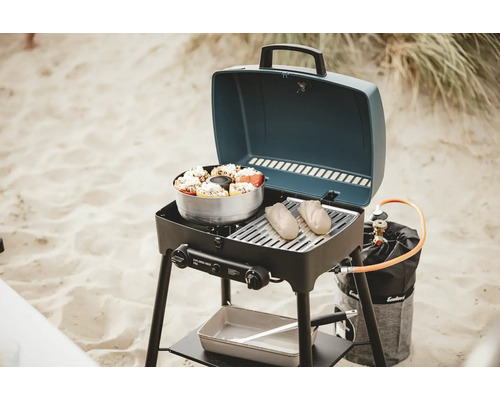 Tragbarer Gasgrill mit Speisen auf dem Grillrost und im Topf