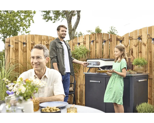Familie bereitet Essen mit einem Pizzaofen im Garten zu.