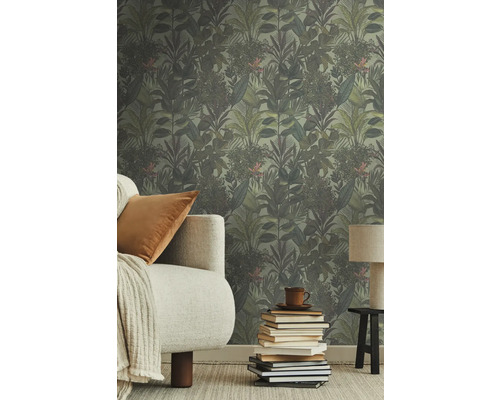 Raum mit Dschungeltapete, Sofa, Kissen, Lampe und Bücherstapel.