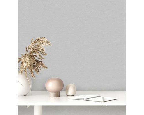 Nahaufnahme einer grauen Textiltapete mit dekorativen Vasen und Notizblock auf einem Tisch.