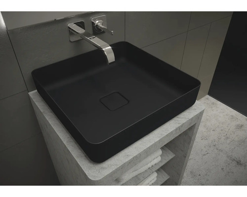 Schwarzes Aufsatzwaschbecken auf einem Waschtisch mit Ablagefächern und Handtüchern.