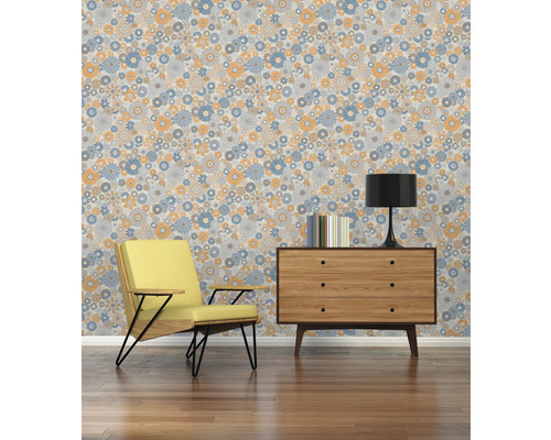 Wohnraum mit Sessel, Kommode, Lampe, Büchern und einer Tapete mit Blumenmuster.