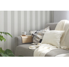 Wohnzimmer mit gestreifter Tapete, Sofa mit Kissen und Decke sowie einem Tablett mit Tasse.