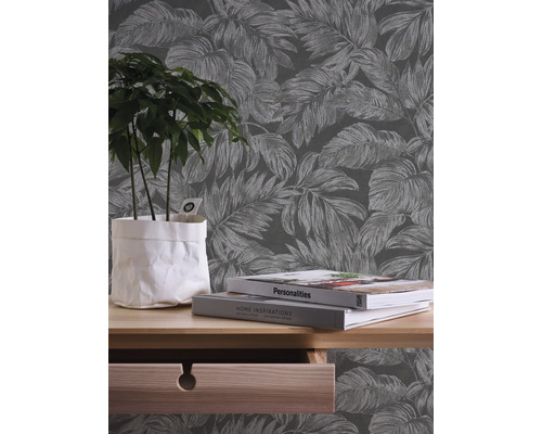 Zimmer mit floral gemusterter Tapete, Pflanze im Topf, Büchern und Kommode