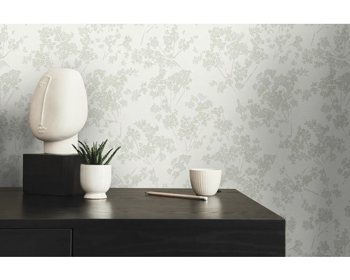 Dekoratives Interieur mit einer gemusterten Tapete, einer Skulptur und einer Zimmerpflanze auf einer Kommode.