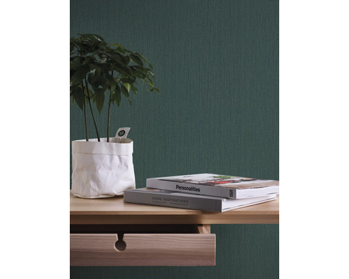 Nahaufnahme eines Zimmers mit einer grünen Tapete, einem Holztisch, Büchern und einer Zimmerpflanze.