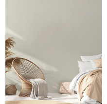 Helles Schlafzimmer mit Rattansessel, Bett und Dekorationen im Boho-Stil.