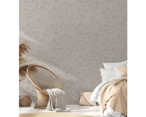 Schlafzimmer mit Rattan-Sessel und Bett vor einer Wand mit Struktur-Tapete.