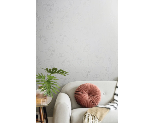 Wohnzimmer mit Tapete mit Frauengesichtern, Sofa, Kissen, Pflanze und Tisch