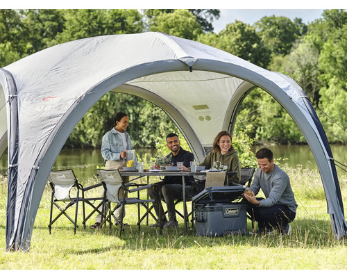 Szene mit Pavillon, Tisch, Stühlen und Kühlbox im Freien, umgeben von Menschen