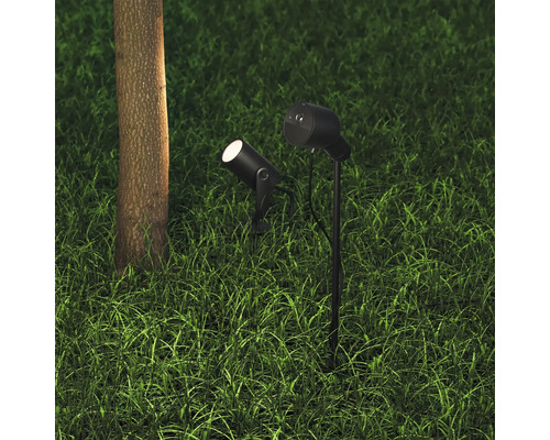 Zwei Gartenstrahler mit Erdspieß im Rasen neben einem Baumstamm.