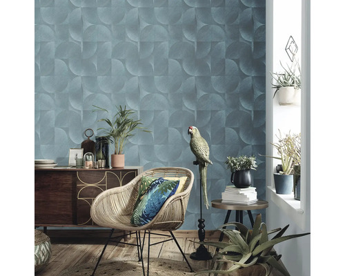 Wohnzimmer mit geometrischer Tapete, Rattansessel, Holzkommode und Zimmerpflanzen