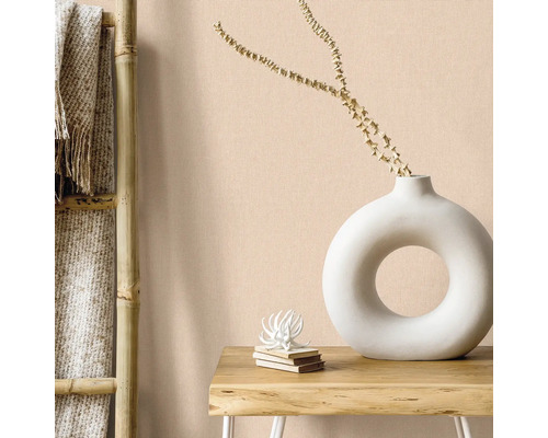 Wohnraum-Szene mit Bambusleiter, Textilien und Dekorationen wie einer weißen Donut-Vase und einem Bücherstapel auf einem Holztisch vor einer einfarbigen Wand.