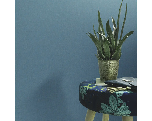 Dekorative Zimmerpflanze in einem verzierten Pflanzgefäß auf einem Hocker vor einer Wand.