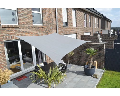 Graues Sonnensegel über einer Terrasse mit Tisch und Pflanzen.