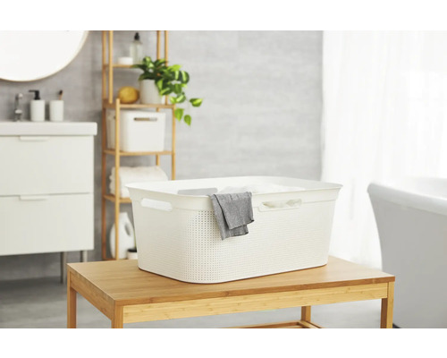 Heller Wäschekorb aus Kunststoff auf einem Holztisch in einem Badezimmer.