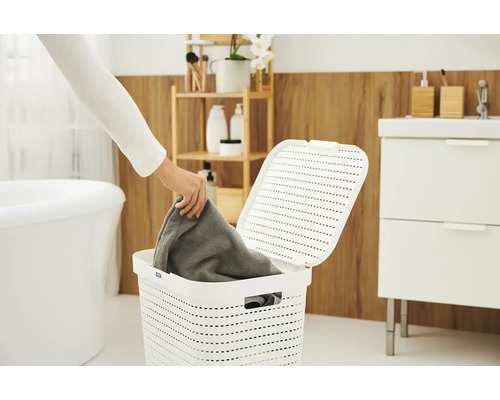 Wäschekorb im Badezimmer mit geöffnetem Deckel und einer Person, die ein Handtuch hineinlegt