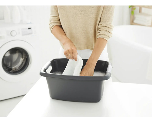 Frau wäscht Wäsche in einer grauen Waschschüssel im Badezimmer