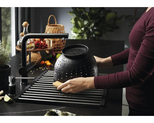 Spüle mit Abtropfgestell, Wasserhahn und Person beim Reinigen eines Siebes