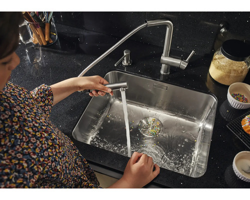 Frau reinigt Spüle mit ausziehbarer Küchenarmatur.