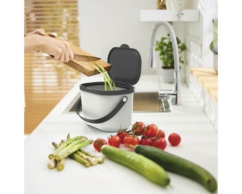 Küchenszene mit Bioabfalleimer, Gemüseresten und schneidender Person