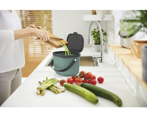 Person entsorgt Gemüsereste in einem Komposteimer auf einer Küchentheke