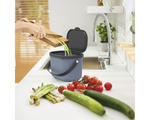 Person wirft Gemüsereste in einen Komposteimer in der Küche.