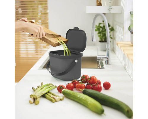 Küchenszene mit Komposteimer, Gemüseresten, Schneidebrett, Messer, Tomaten, Gurken und Spargel