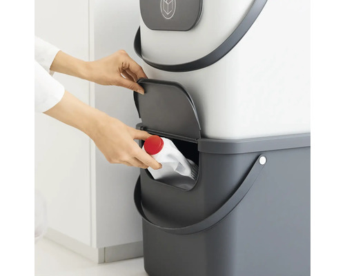 Frau wirft leere Flasche in einen grauen Recyclingeimer