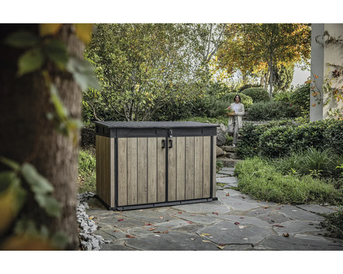 Gartengeräteschrank mit Holzeffekt und Frau im Hintergrund in Gartenlandschaft