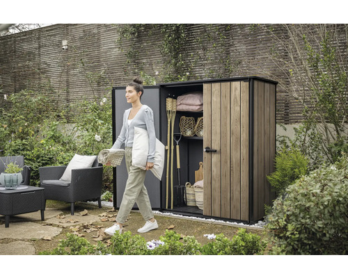 Gartenszene mit Frau vor Gerätehaus mit Gartengeräten und Gartenmöbeln