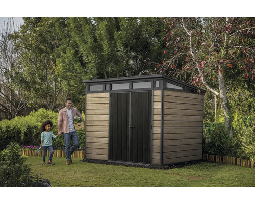 Gartenszene mit Gerätehaus, Mann und Kind auf Rasenfläche.