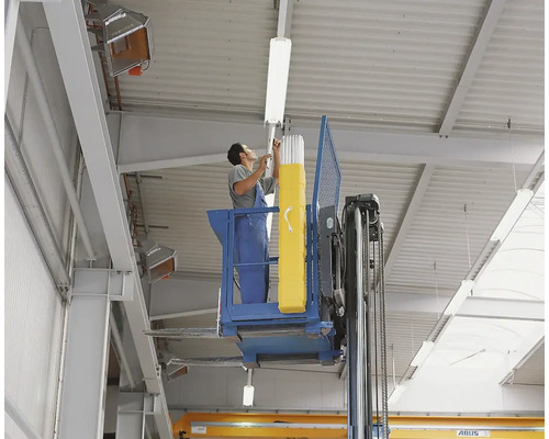 Ein Mann montiert mit einer Hebebühne eine Leuchtstoffröhre in einer Industriehalle.