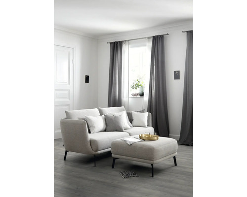 Wohnzimmer mit Sofa, Kissen, Hocker und Vorhängen