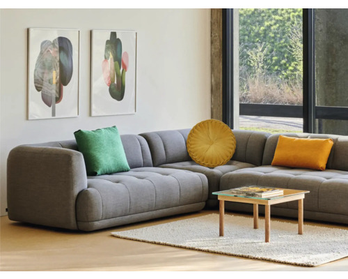 Graues Ecksofa mit Kissen, Couchtisch und Wanddekoration in einem hellen Wohnzimmer.