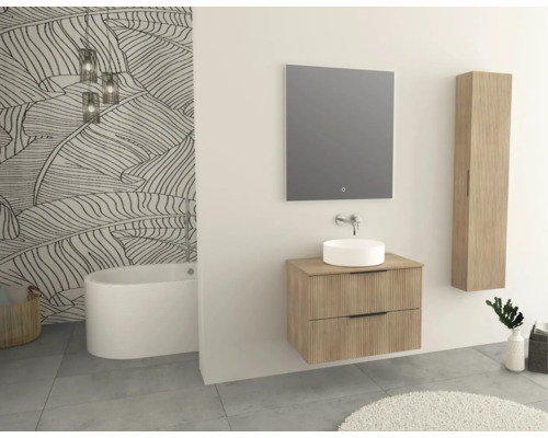 Badezimmer mit Badewanne, Waschtisch, Spiegel und Hängeschrank in hellem Holzdekor vor einer mit Blättern gemusterten Tapete.