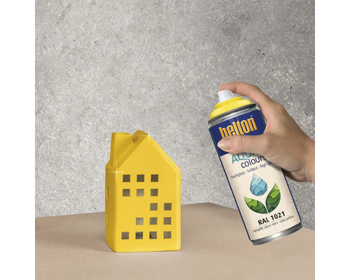 Eine Person sprüht ein gelbes Deko-Haus mit Helton Aqua Colours Sprühlack RAL 1021.