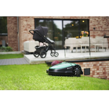 Rasenmähroboter auf einer Rasenfläche, im Hintergrund ein Kinderwagen und ein Haus.